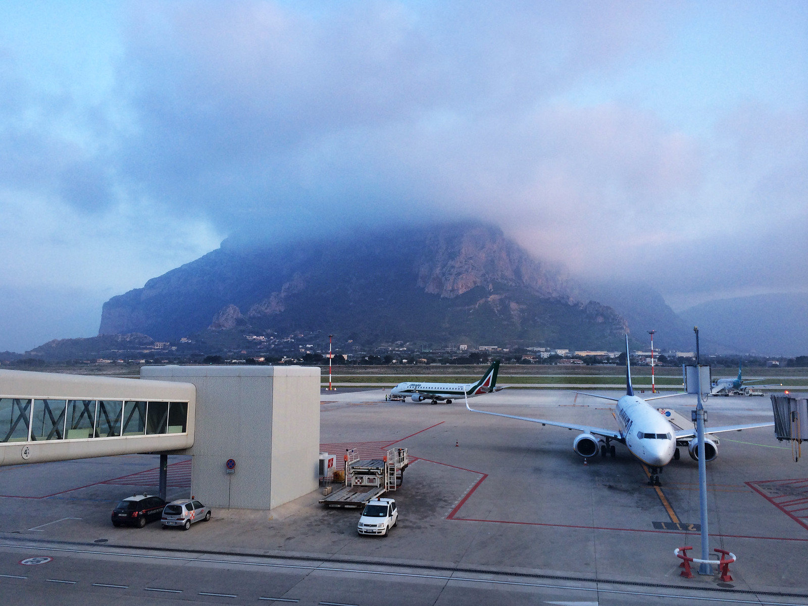 Aerei parcheggiati sul piazzale dell'aeroporto di Palermo con la montagna avvolta dalle nuvole sullo sfondo
