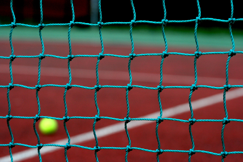 Pallina da tennis vista attraverso la rete su un campo in terra rossa